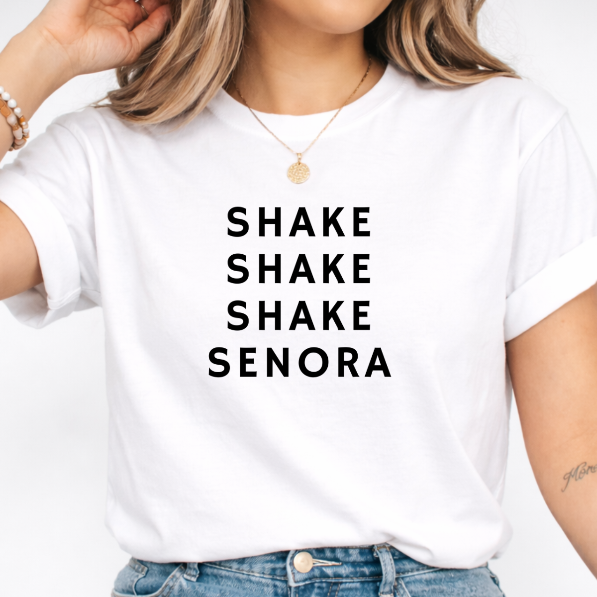 Woman wearing a white Shake Shake Shake Señora Halloween graphic tee with black lettering.