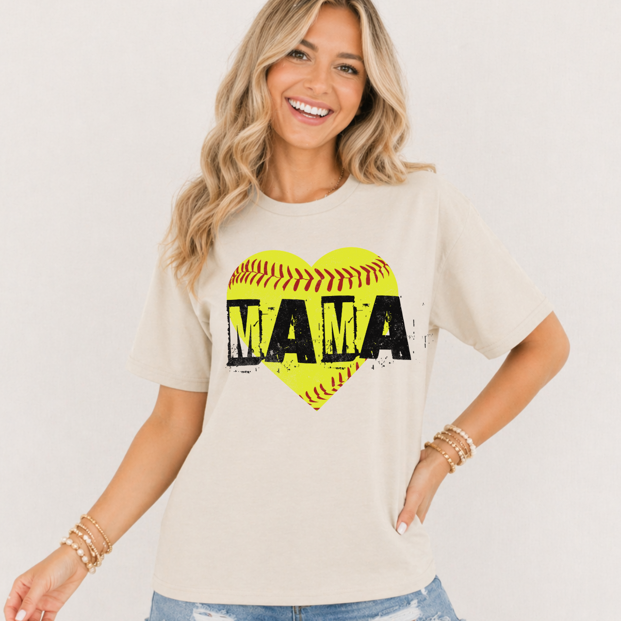 Woman wearing a beige t-shirt with a heart-shaped softball design and 'MAMA' text.