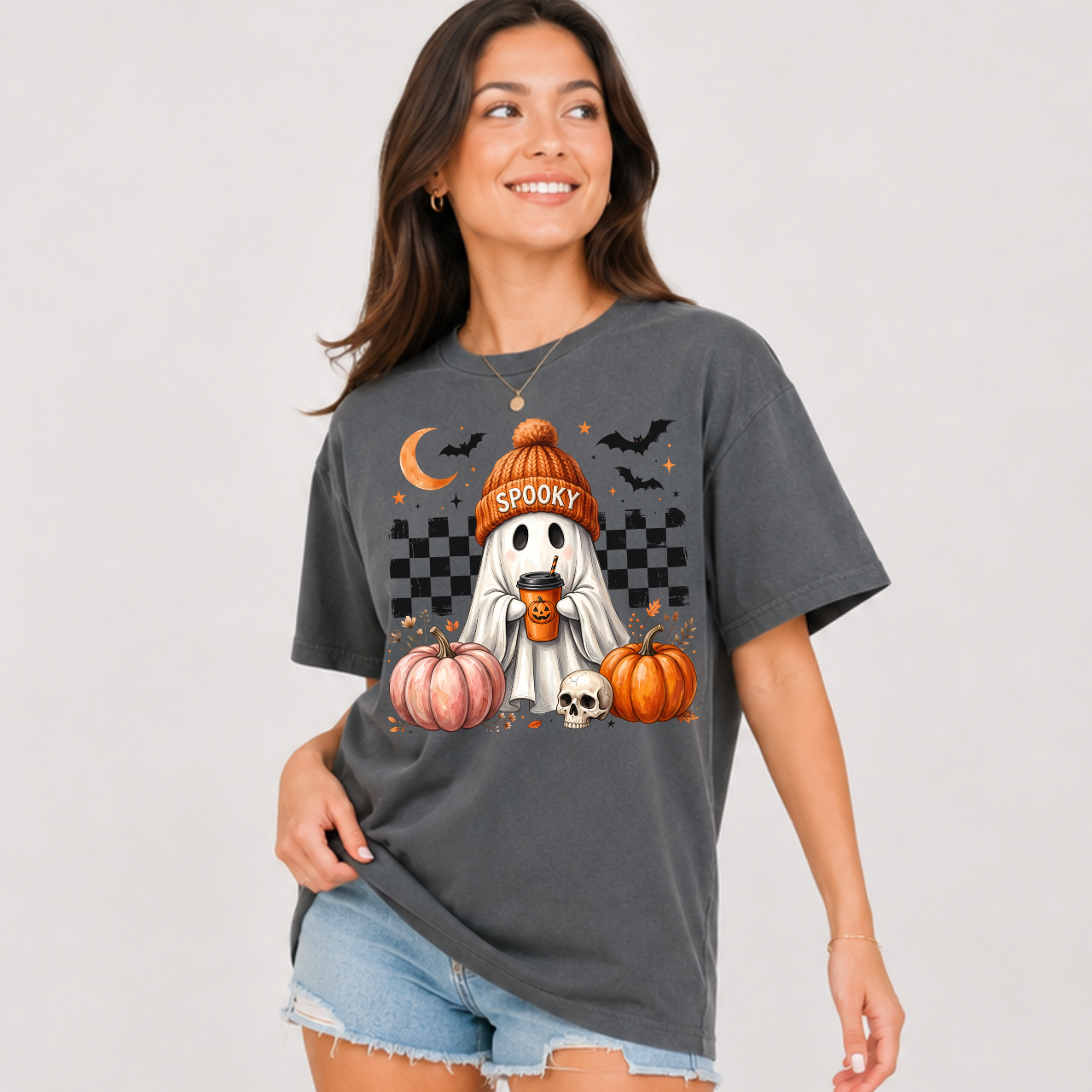 Woman wearing a gray charcoal spooky ghost pumpkin coffee graphic tee with pumpkins, bats, and a ghost in an orange beanie