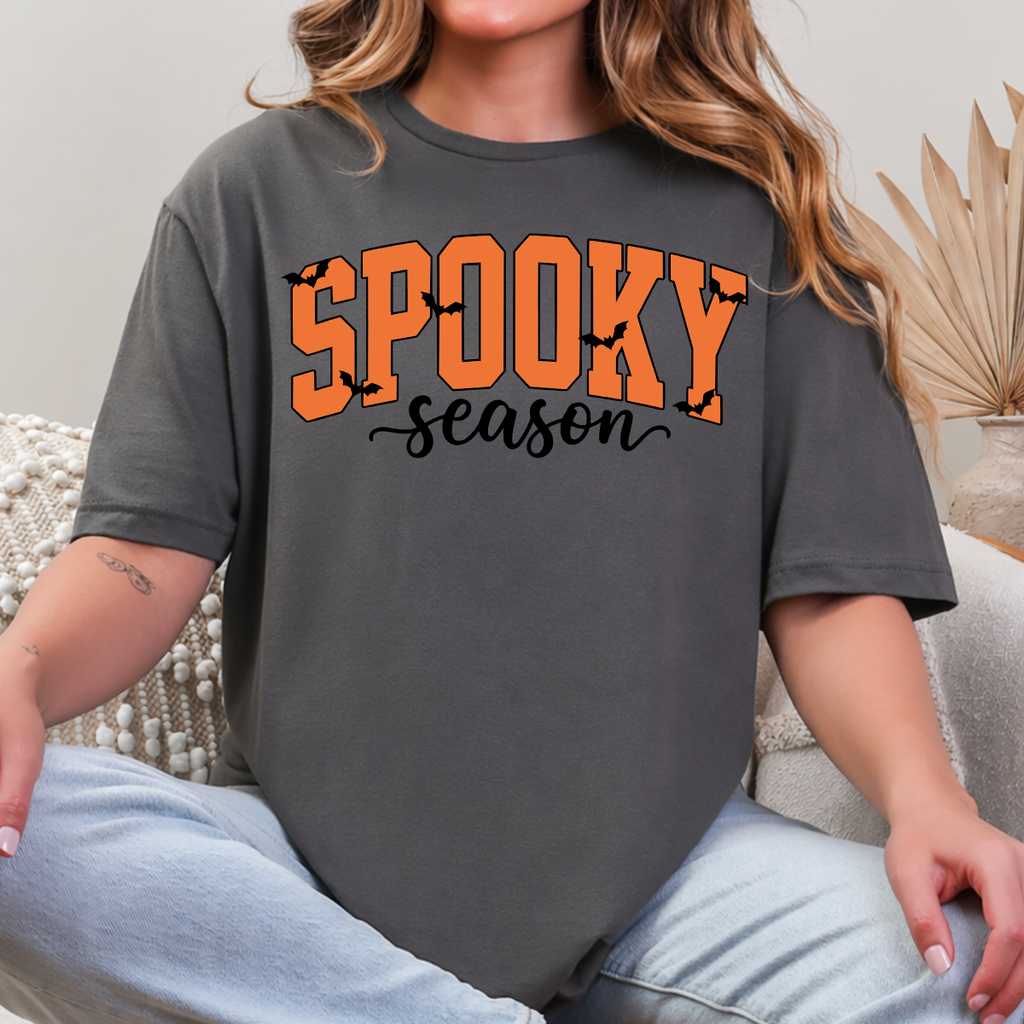 Woman wearing a charcoal Spooky Season Halloween graphic tee with orange lettering and black bats.