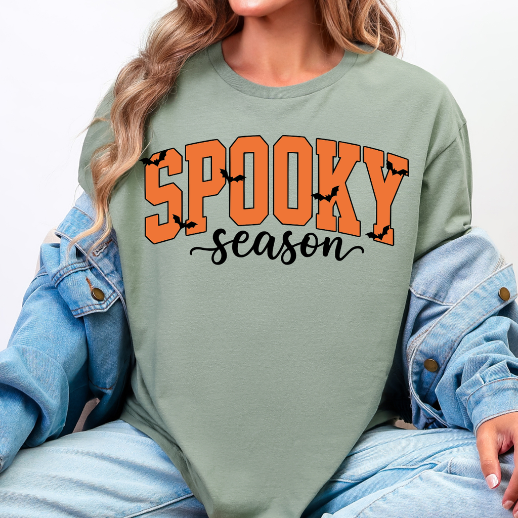 Woman wearing a sage Spooky Season Halloween graphic tee with orange lettering and black bats.