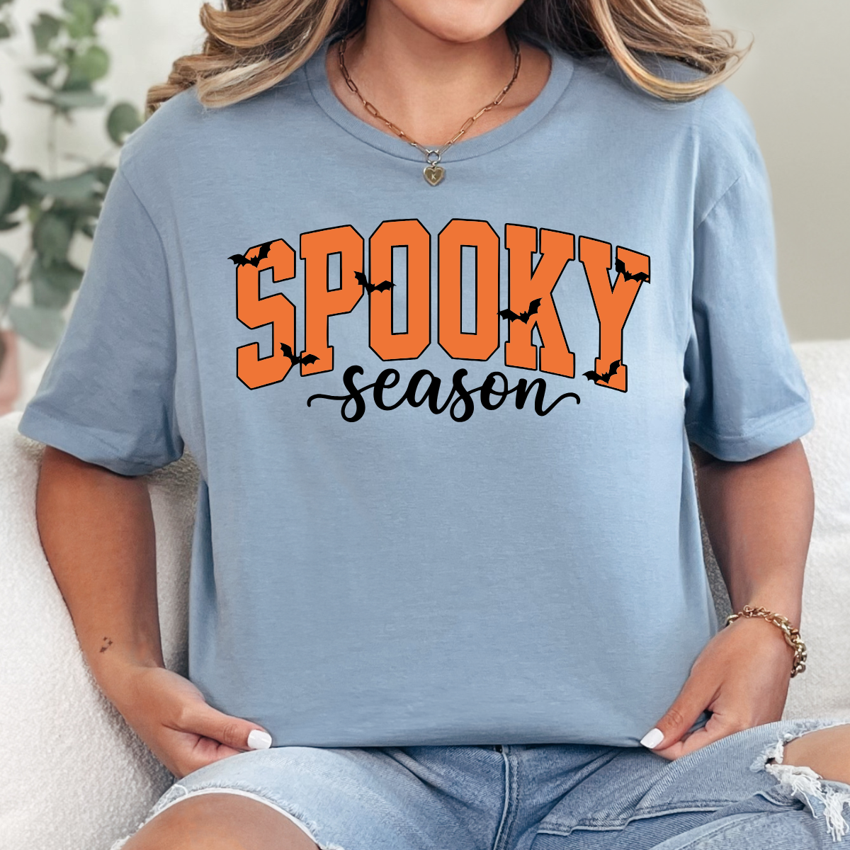 Woman wearing a stone blue Spooky Season Halloween graphic tee with orange lettering and black bats.