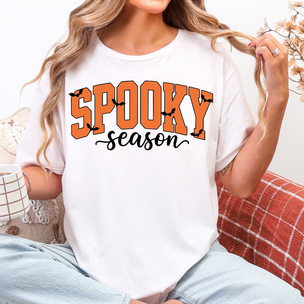 Woman wearing a white Spooky Season Halloween graphic tee with orange lettering and black bats.