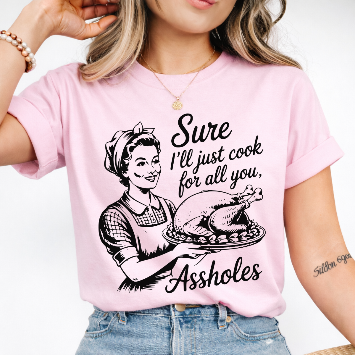Woman wearing a pink funny Thanksgiving graphic tee with a retro hostess holding a roasted turkey.