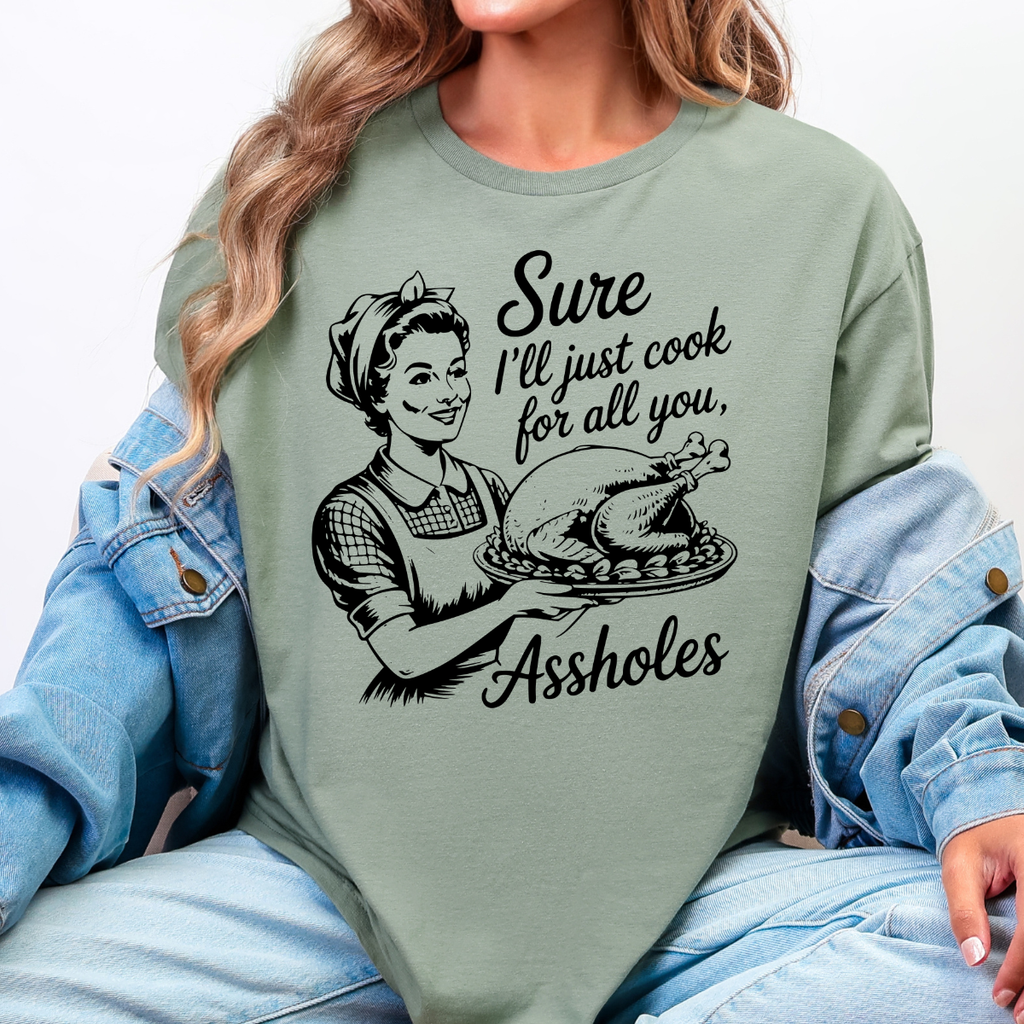 Woman wearing a sage green funny Thanksgiving graphic tee with a retro hostess holding a roasted turkey