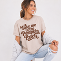 Woman wearing a sand Take Me to the Pumpkin Patch graphic tee with brown retro lettering.