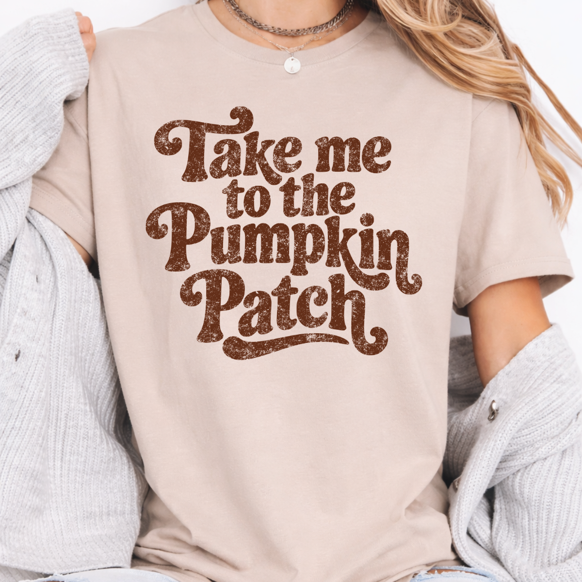 Woman wearing a sand Take Me to the Pumpkin Patch graphic tee with brown retro lettering
