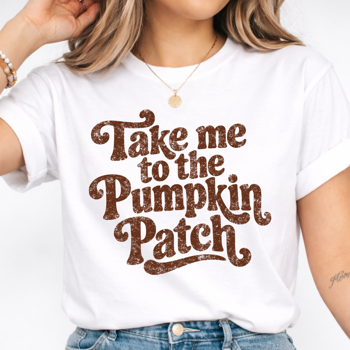 Woman wearing a white Take Me to the Pumpkin Patch graphic tee with brown retro lettering.