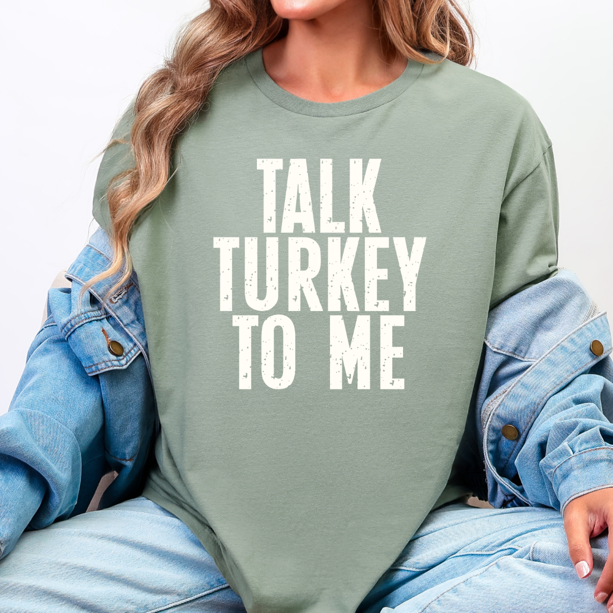 Woman wearing a sage green Talk Turkey to Me Thanksgiving graphic tee with distressed brown lettering