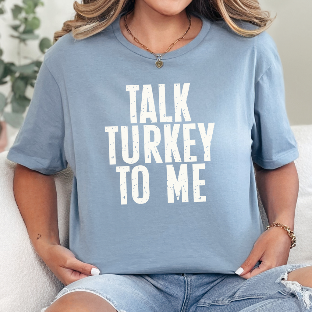 Woman wearing a stone blue Talk Turkey to Me Thanksgiving graphic tee with distressed brown lettering