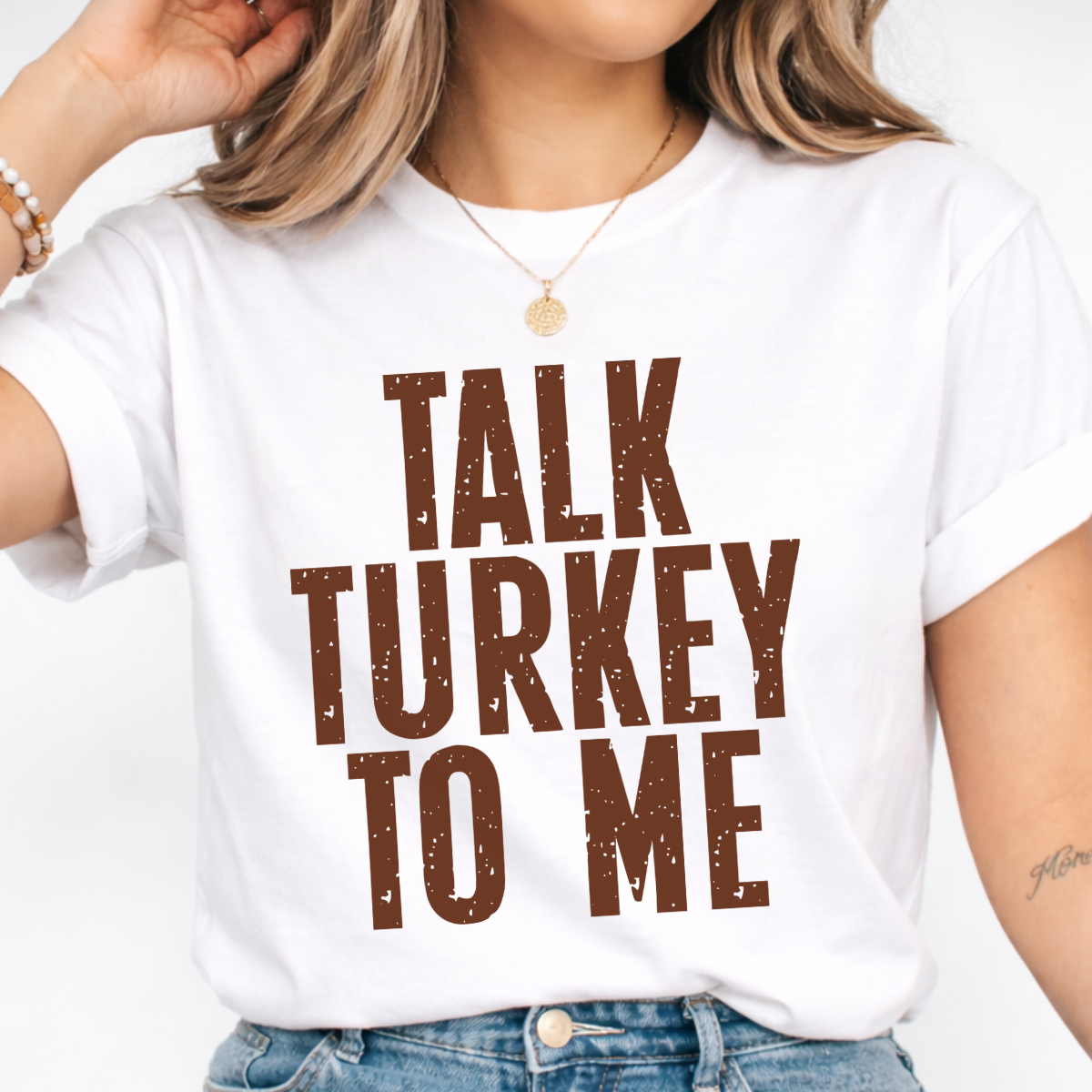 Woman wearing a white Talk Turkey to Me Thanksgiving graphic tee with distressed brown lettering