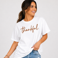 Woman wearing a white Thankful Thanksgiving graphic tee with warm brown script lettering.