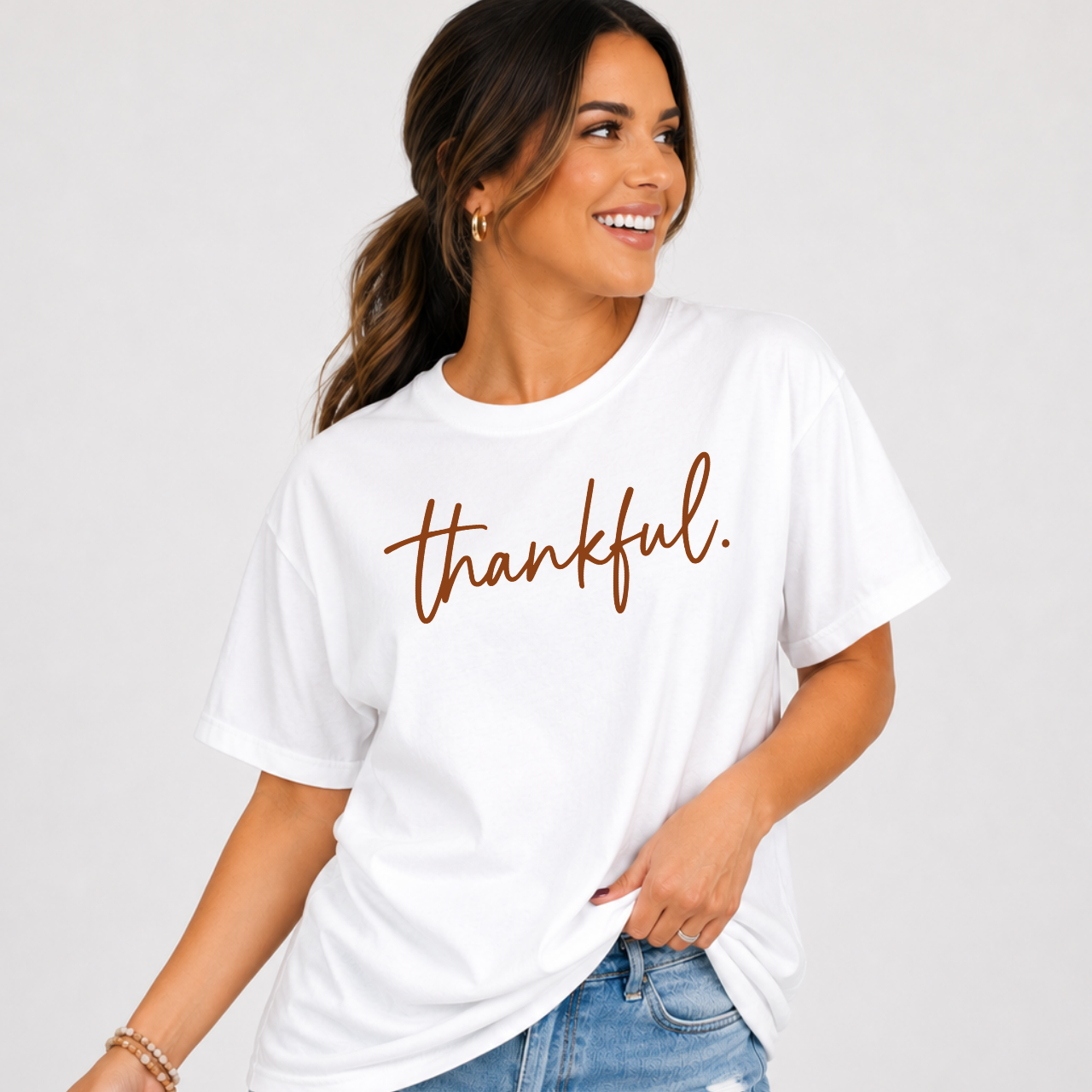 Woman wearing a white Thankful Thanksgiving graphic tee with warm brown script lettering.