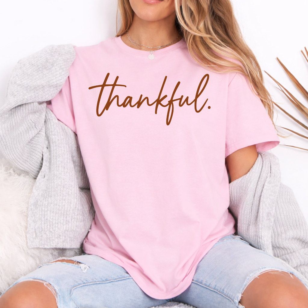 Woman wearing a light pink Thankful Thanksgiving graphic tee with warm brown script lettering.