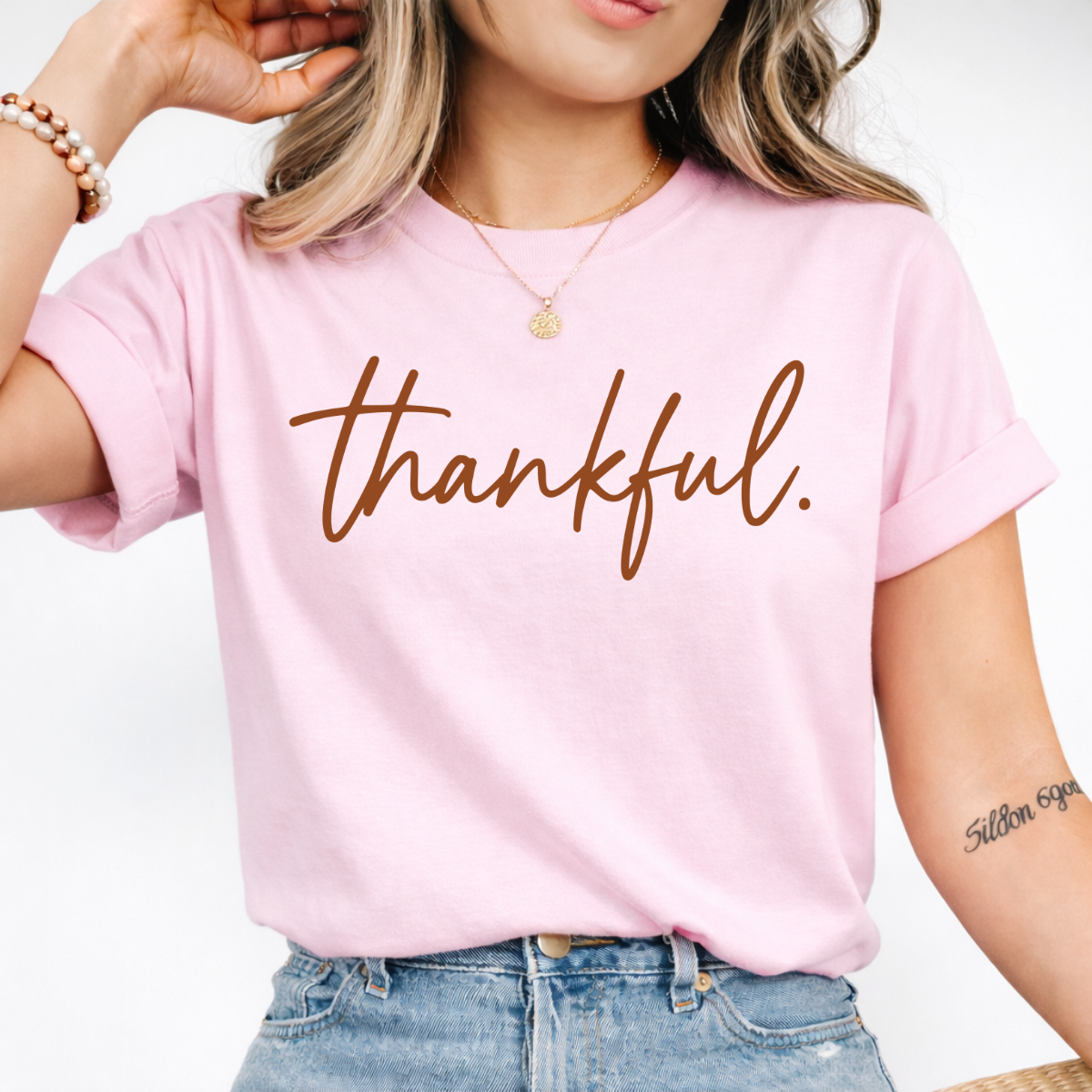 Woman wearing a light pink Thankful Thanksgiving graphic tee with warm brown script lettering.