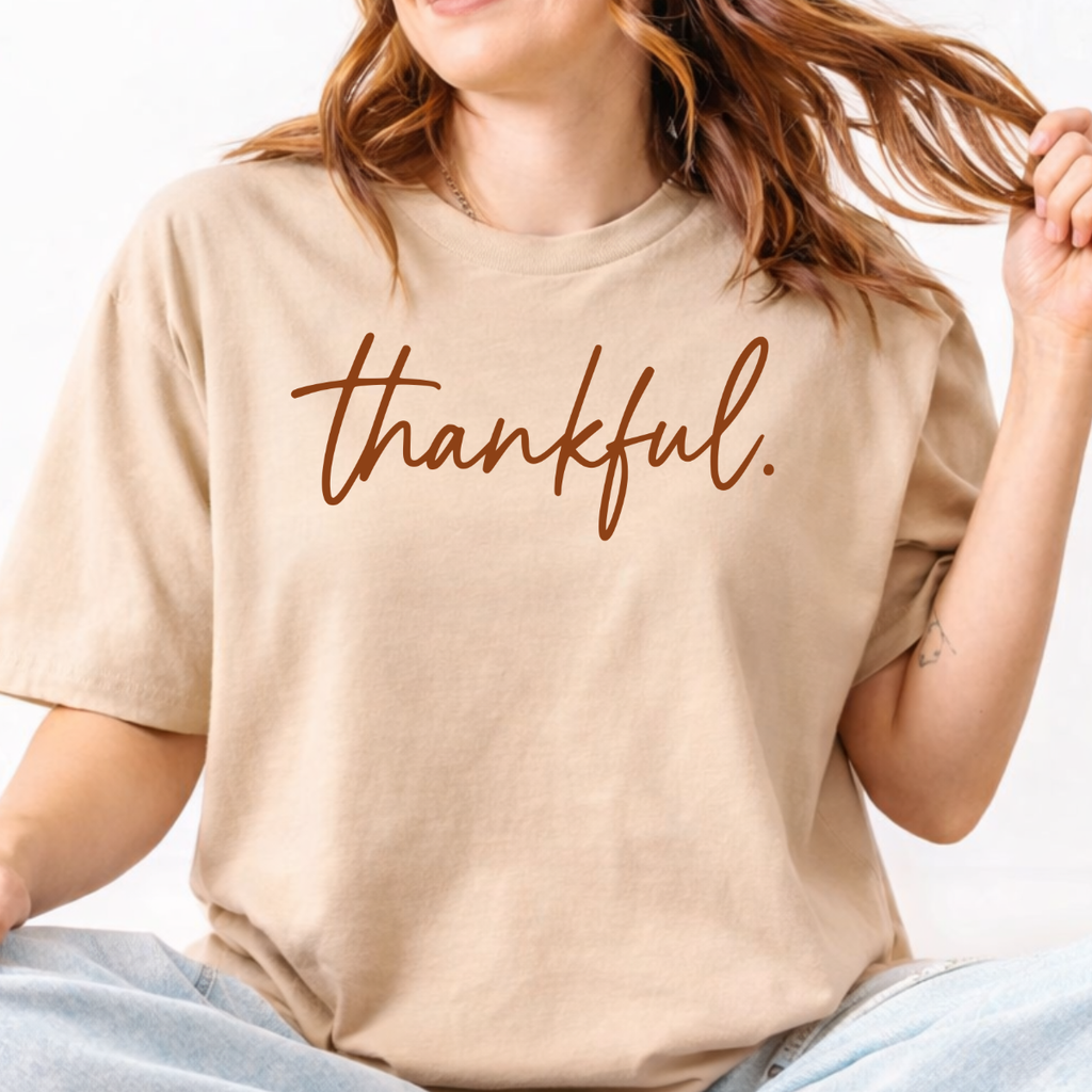 Woman wearing a Sand Thankful Thanksgiving graphic tee with warm brown script lettering.