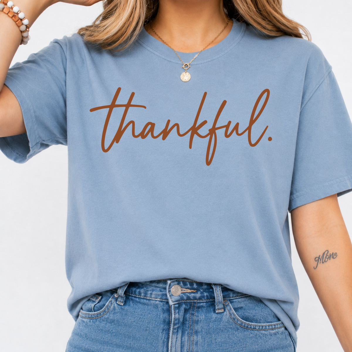 Woman wearing a stone blue Thankful Thanksgiving graphic tee with warm brown script lettering.