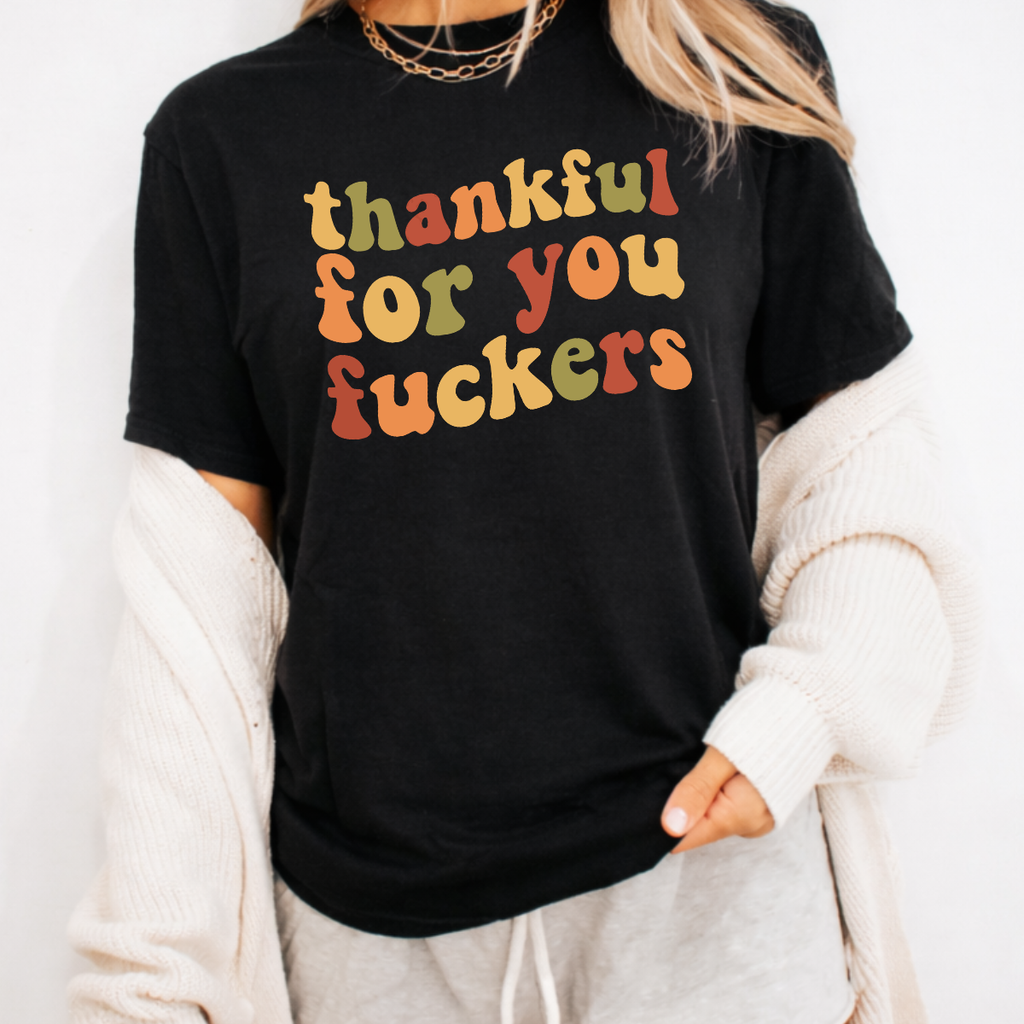 Woman wearing a black Thankful for You Fuckers Thanksgiving graphic tee with colorful retro lettering.