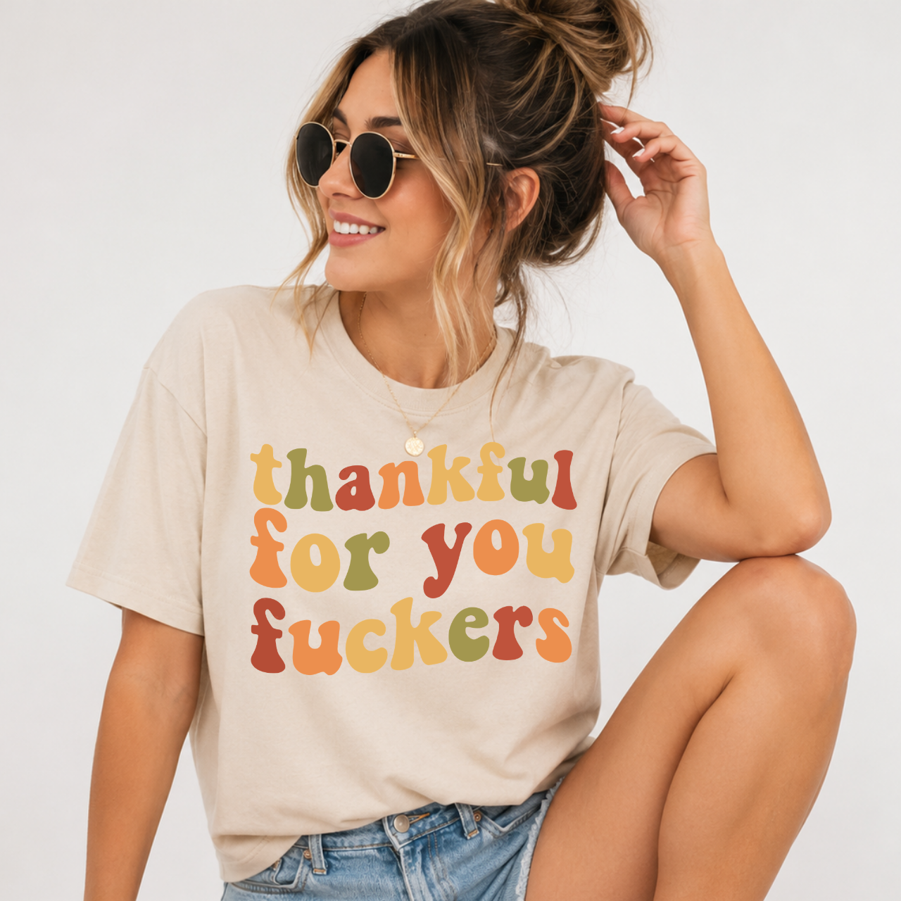 Woman wearing a sand Thankful for You Fuckers Thanksgiving graphic tee with colorful retro lettering.