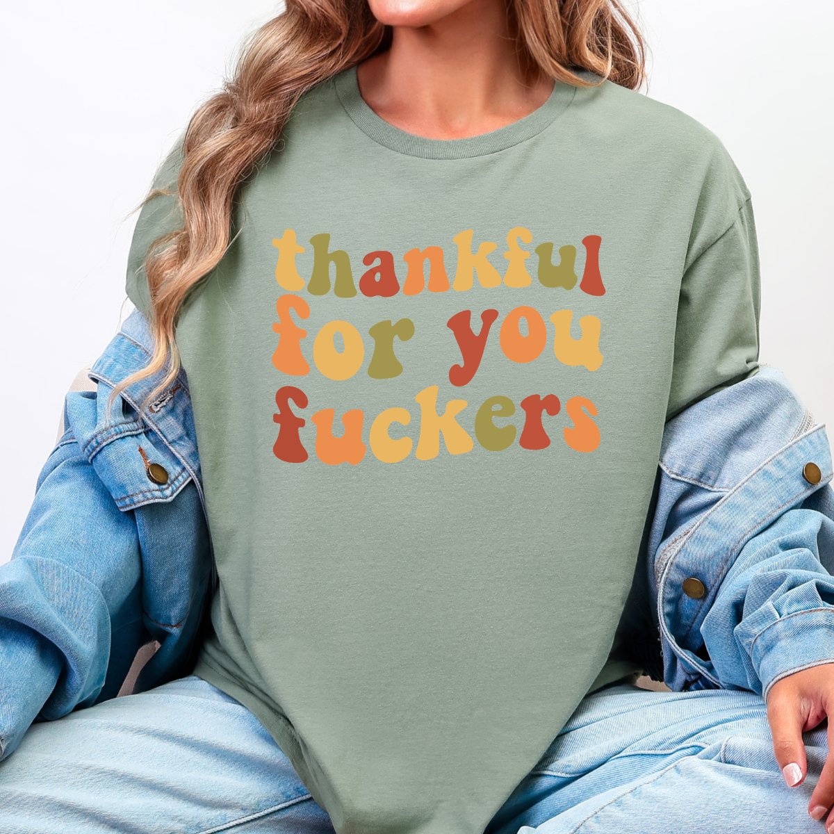 Woman wearing a sage Thankful for You Fuckers Thanksgiving graphic tee with colorful retro lettering.