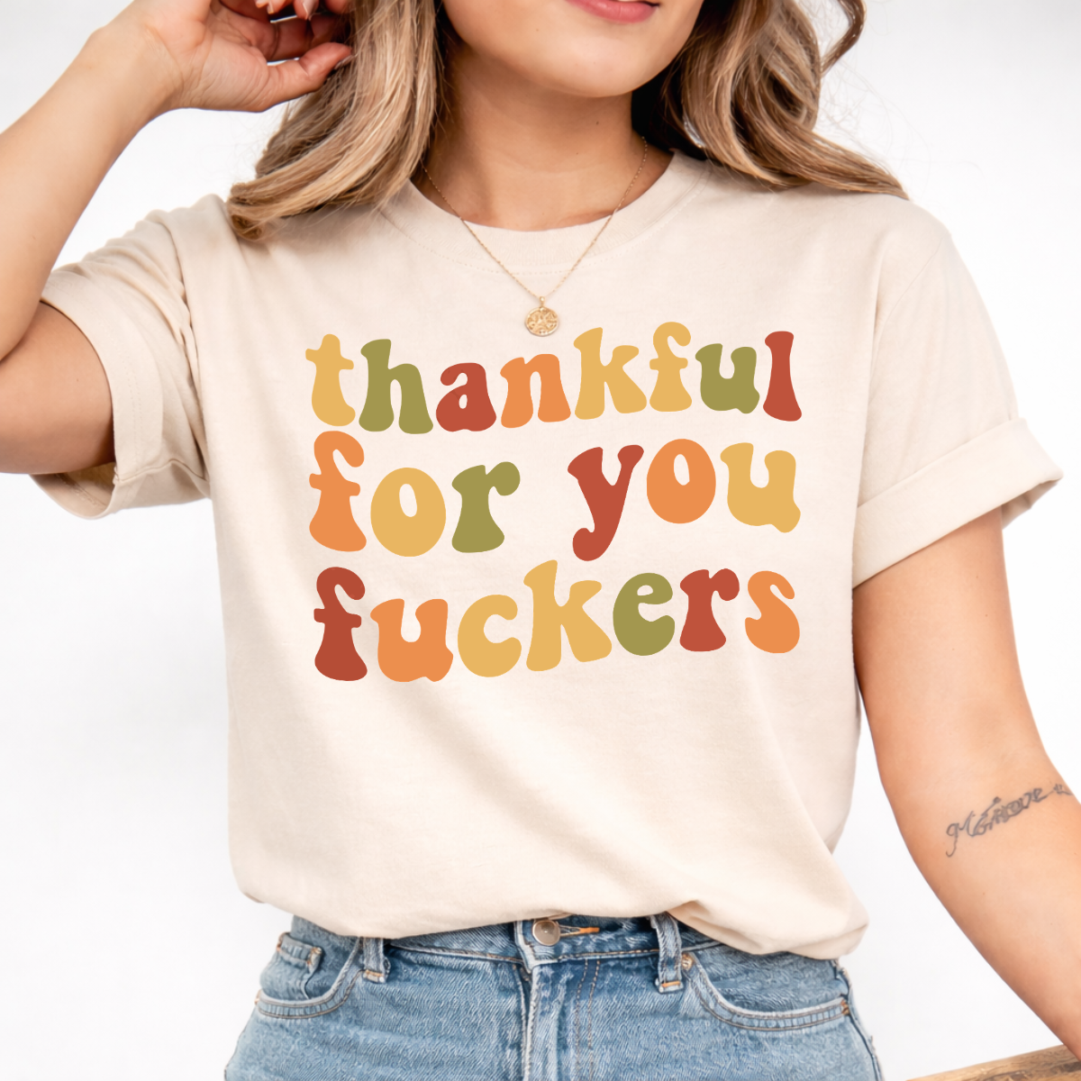 Woman wearing a sand Thankful for You Fuckers Thanksgiving graphic tee with colorful retro lettering.