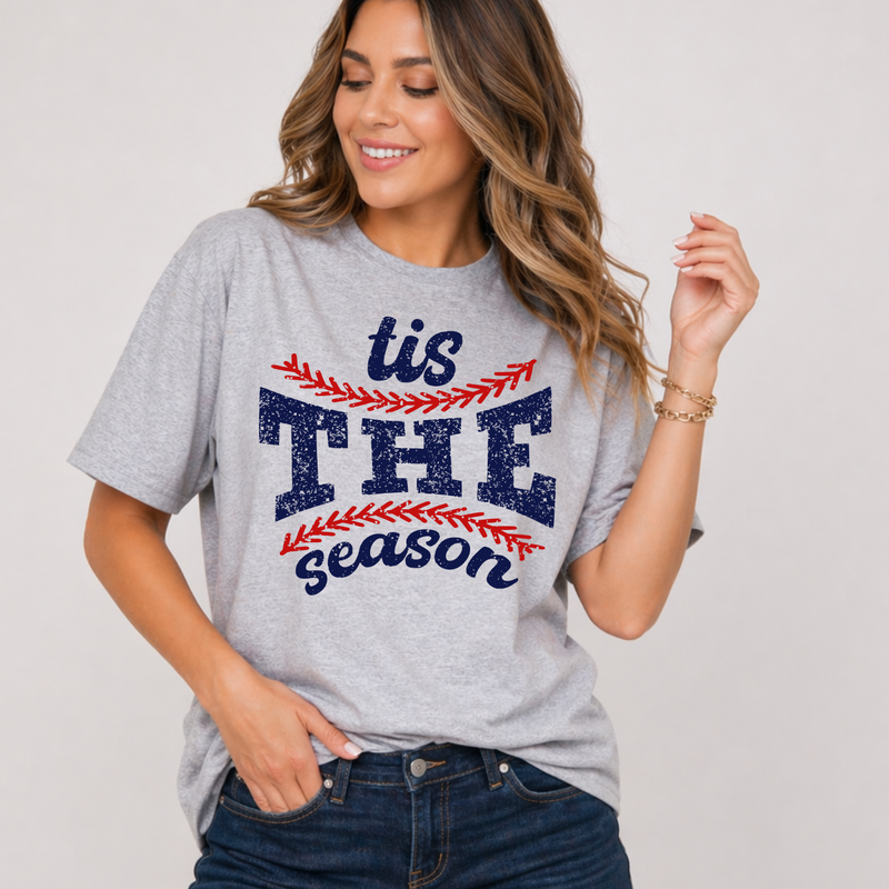Woman wearing a gray t-shirt with 'tis THE season' text and baseball elements on a plain background
