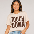 Woman wearing a cream Touchdown football graphic tee with bold brown distressed lettering