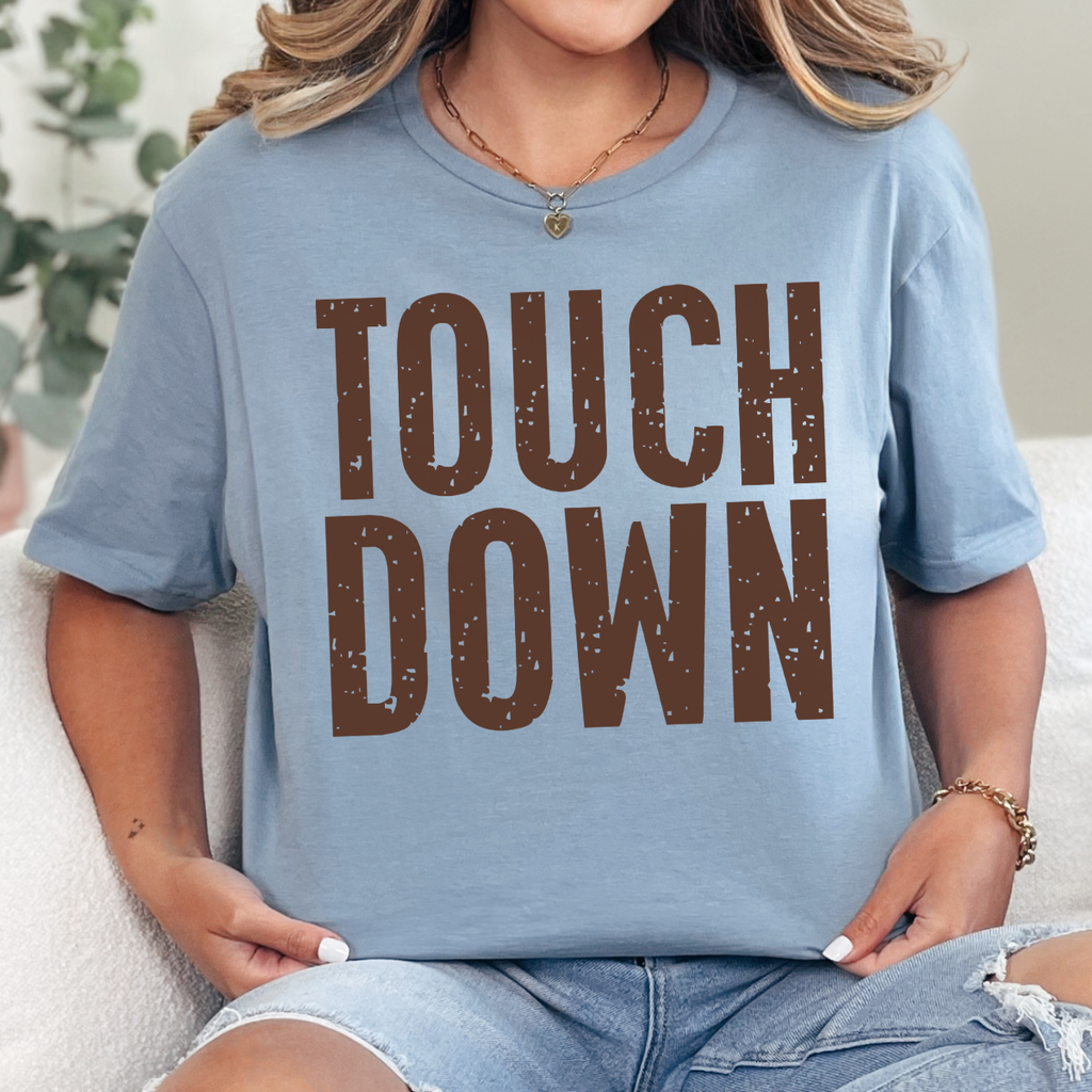 Woman wearing a stone blue Touchdown football graphic tee with bold brown distressed lettering