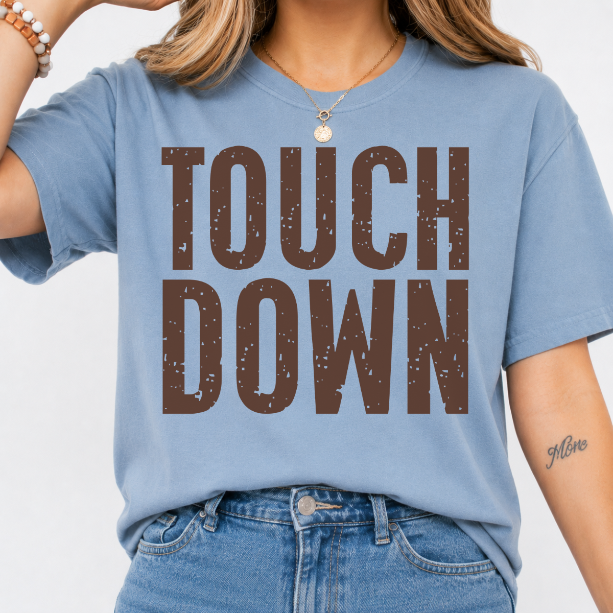 Woman wearing a stone blue Touchdown football graphic tee with bold brown distressed lettering
