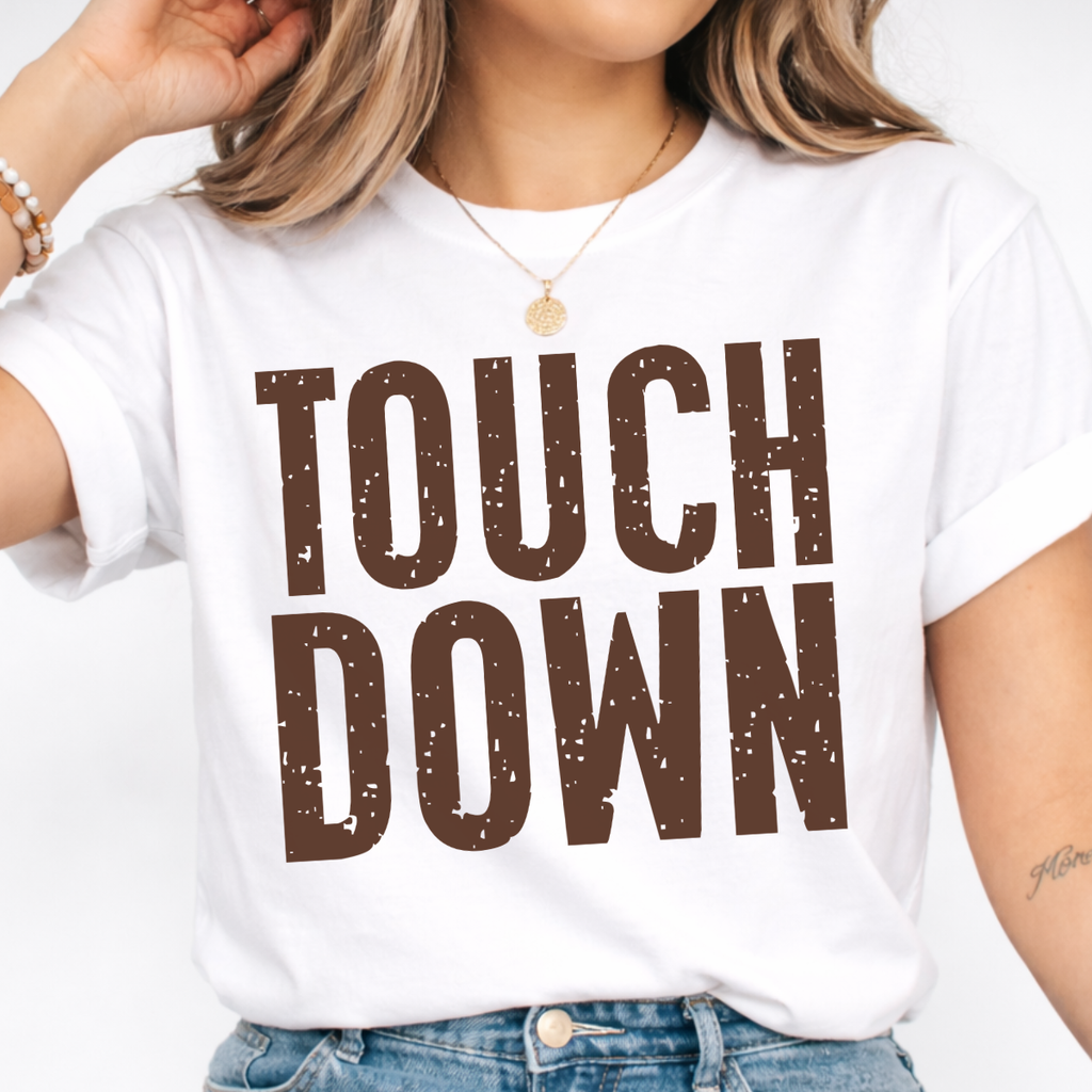 Woman wearing a white Touchdown football graphic tee with bold brown distressed lettering