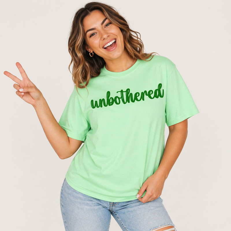 Woman wearing a light green t-shirt with 'unbothered' text, making a peace sign.
