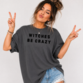 Woman wearing a charcoal Witches Be Crazy Halloween graphic tee with black lettering.