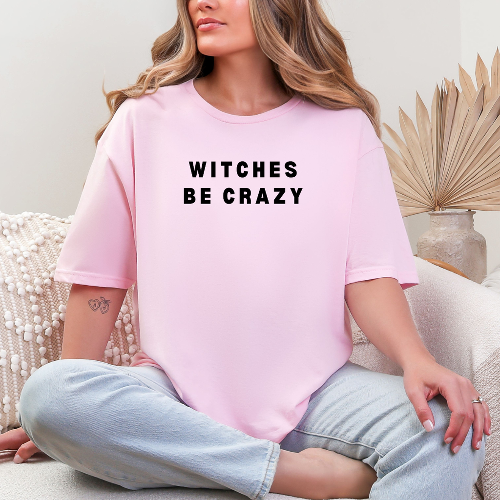 Woman wearing a light pink Witches Be Crazy Halloween graphic tee with black lettering.