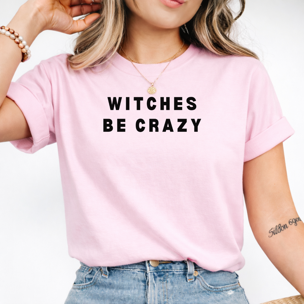 Woman wearing a pink Witches Be Crazy Halloween graphic tee with black lettering.