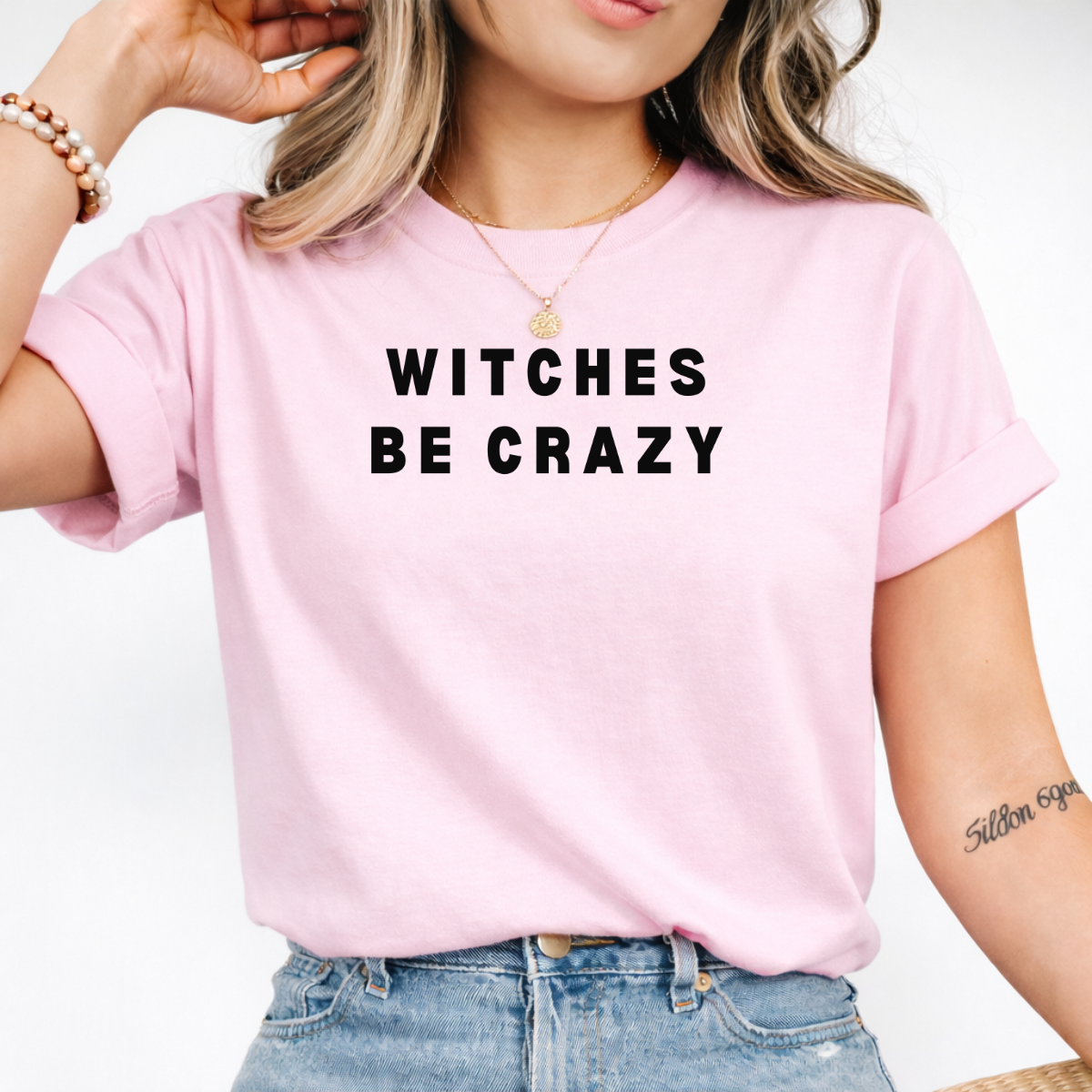 Woman wearing a pink Witches Be Crazy Halloween graphic tee with black lettering.