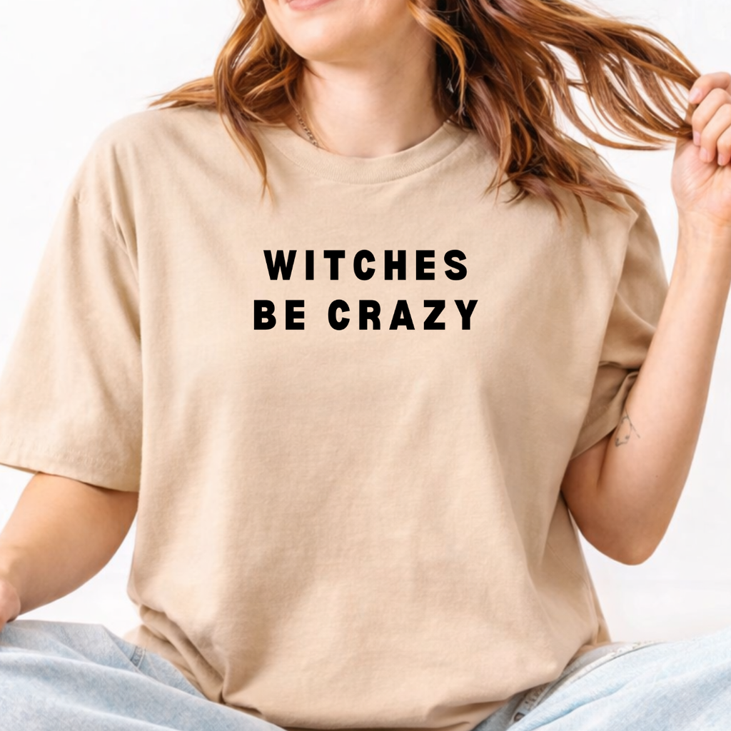 Woman wearing a sand Witches Be Crazy Halloween graphic tee with black lettering.